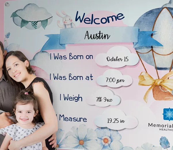 family poses for photo in front of celebration board at hospital