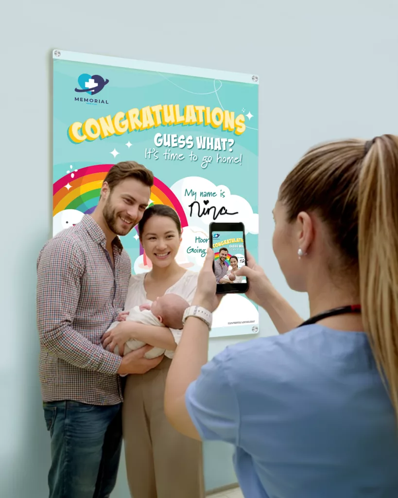 nurse takes photo of new family in front of Mother Baby Discharge Celebration Board